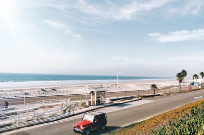 白天在海边公路上行驶的红色汽车